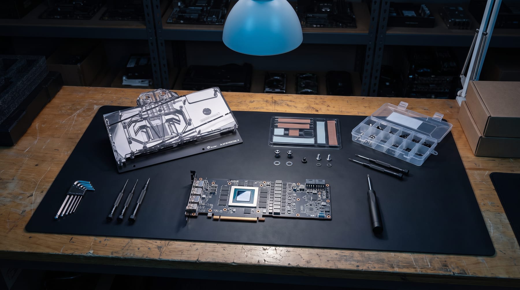 A technician's bench with a Bykski clear GPU water block, a bare graphics card, thermal pads and tools